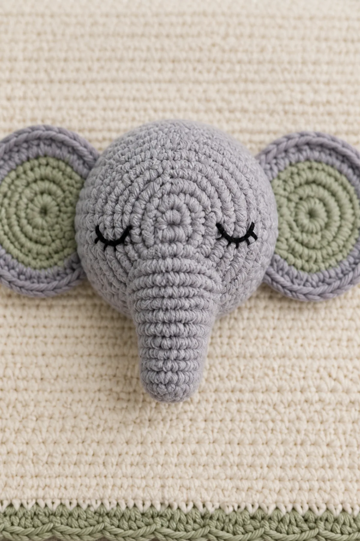 Close-up of the centered elephant's embroidered face, symmetrical flat ears, and anchored short trunk