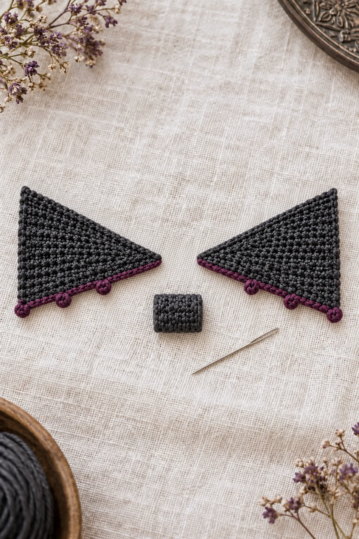 Two separate flat charcoal crochet wing wedges laid as mirrored pair with narrow tips facing each other across a clear gap, broad ends outward, each lower slope edged plum with three tiny picot points, upper edges plain, separate small charcoal rectangular center wrap beside them and sewing needle. Not assembled, no eyes or stuffed body