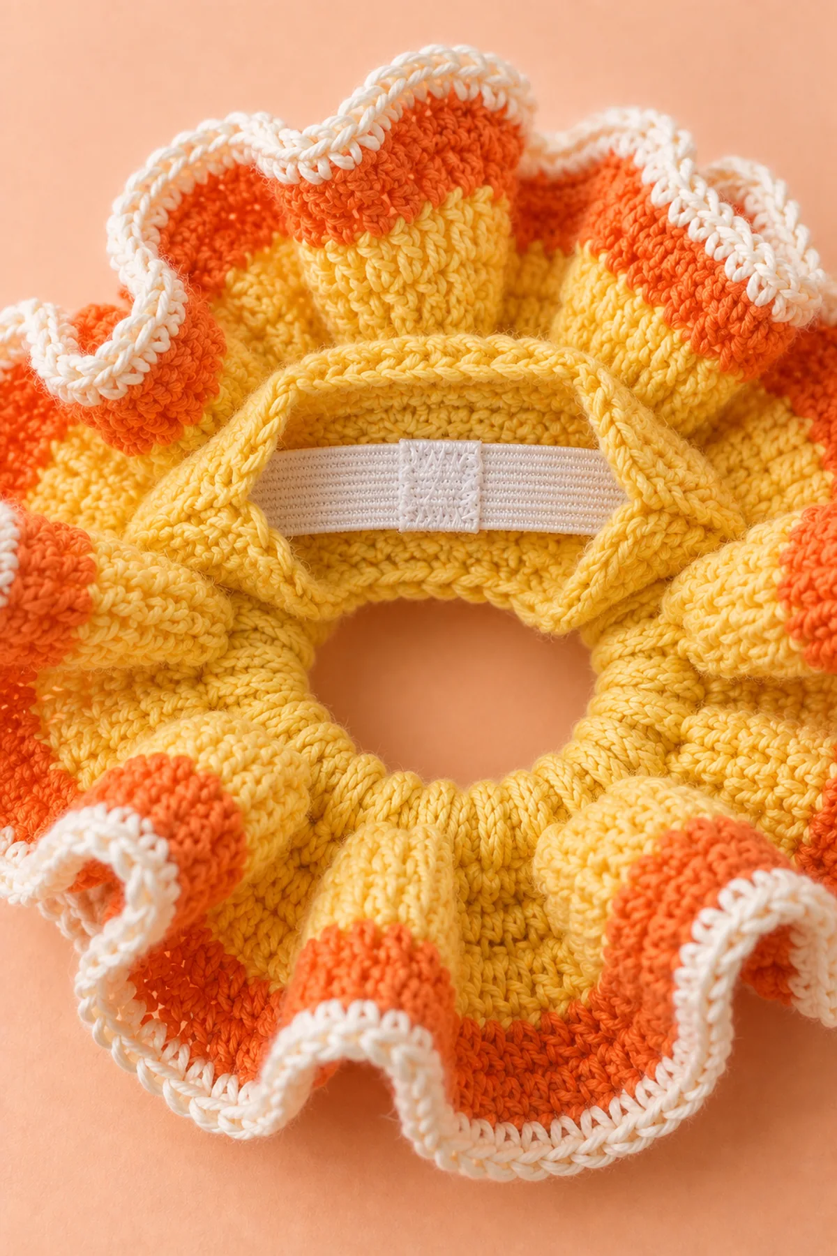Macro on inside yellow crochet casing of candy-corn-colored curly scrunchie: small six-row service opening lifted to reveal white flat elastic with neatly sewn overlapped join, orange ruffle and narrow cream outer edge around background. No safety pin left in casing