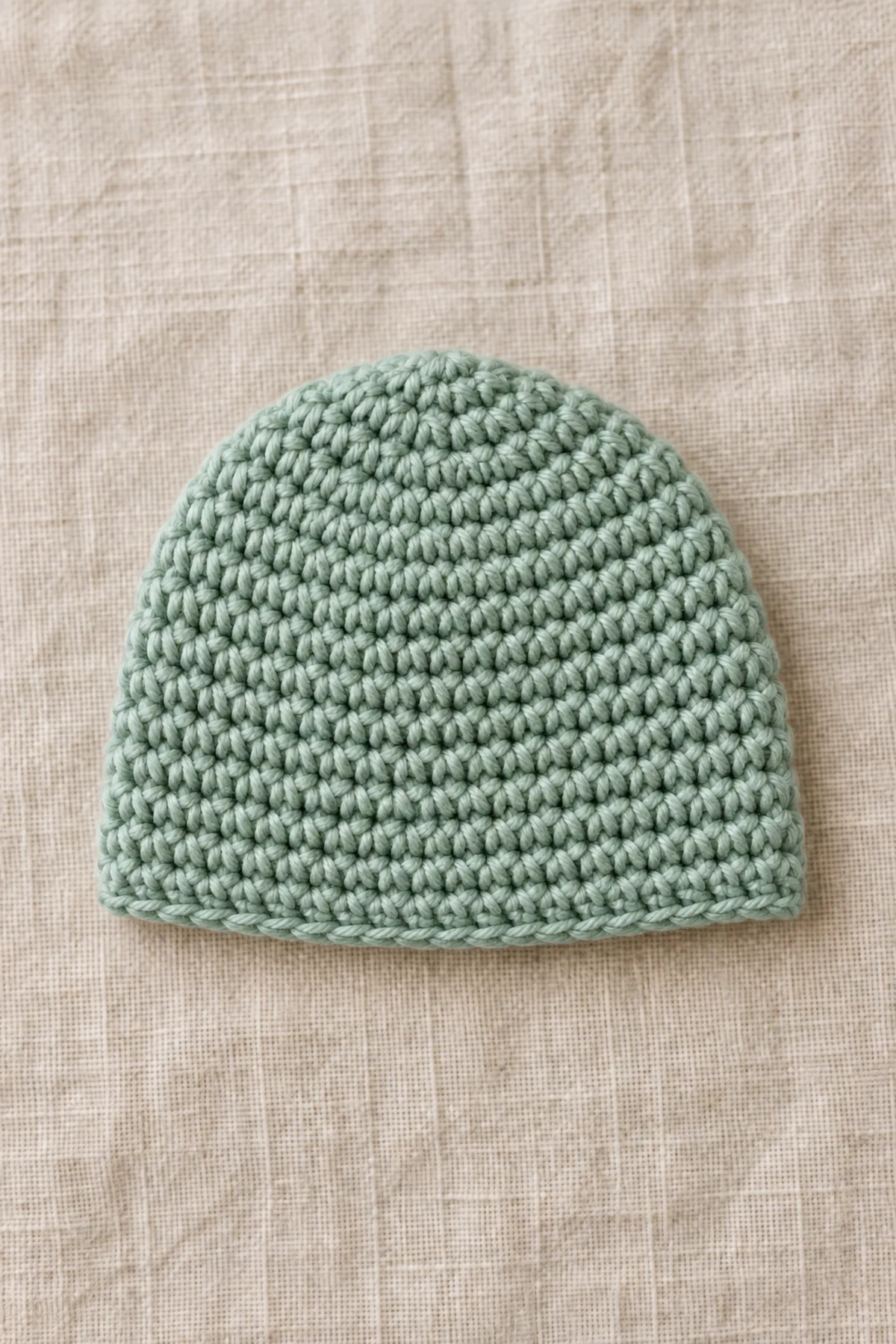 Sea-glass green newborn beanie after the 40-stitch crown and straight depth rounds, before ivory edging