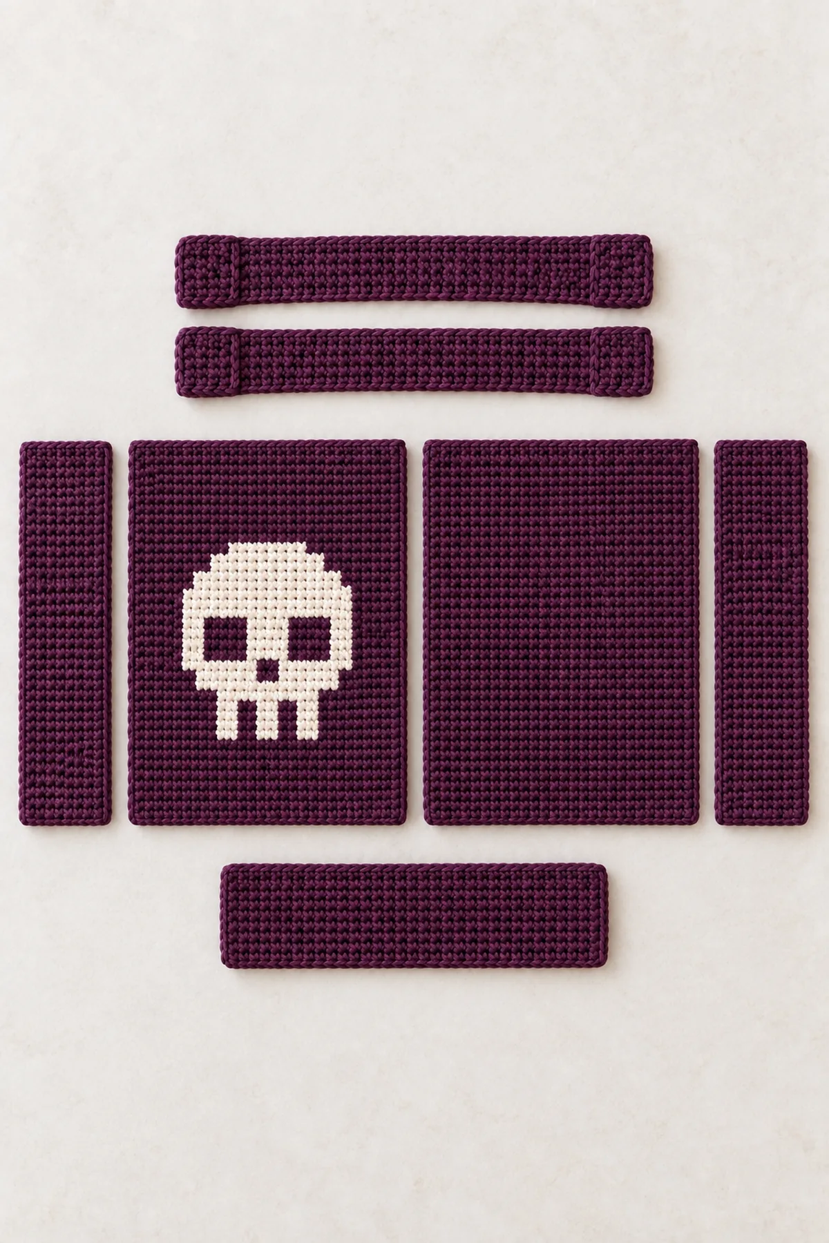 Five aubergine crochet tote pieces laid out before assembly: skull front, plain back, narrow rectangular base and two slim upright side gussets; two separate short wide straps nearby