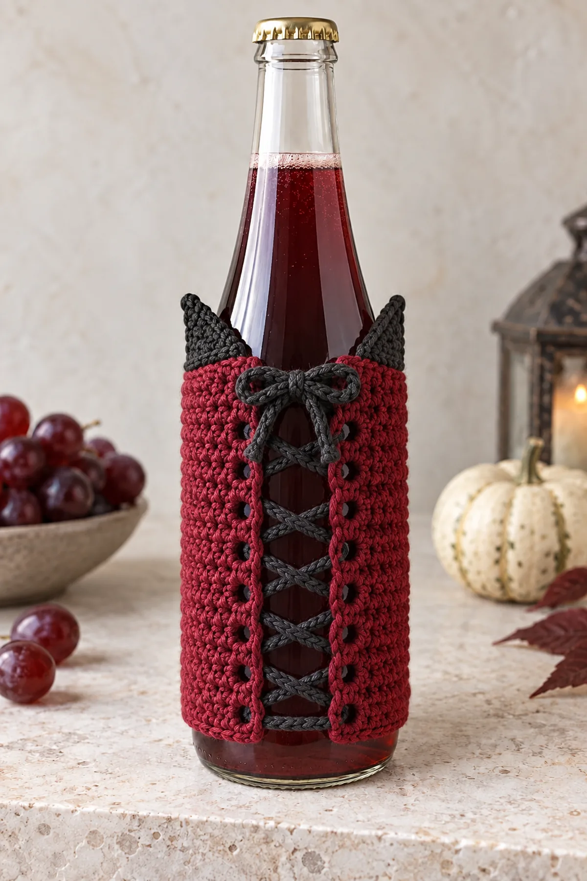 Rear close-up of wine-red crochet bottle wrap showing charcoal cord crisscrossing between matched side eyelet borders with small open gap and a small tied bow at top; part of clear bottle visible, no bottom or handle