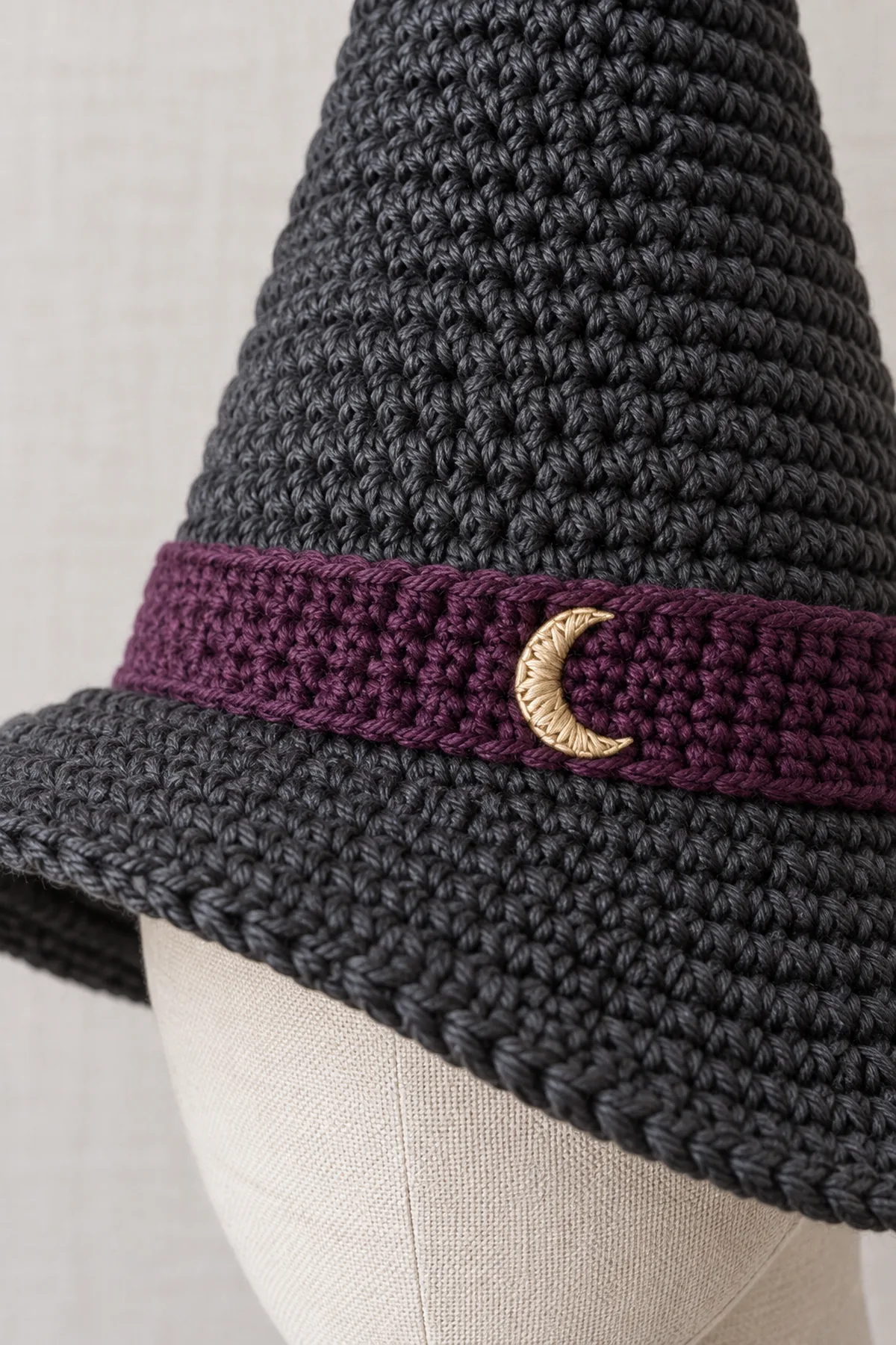 Close view of plum crochet band sewn to charcoal hat base, six small gold stitches forming a crescent, and dense wire-free brim stitches