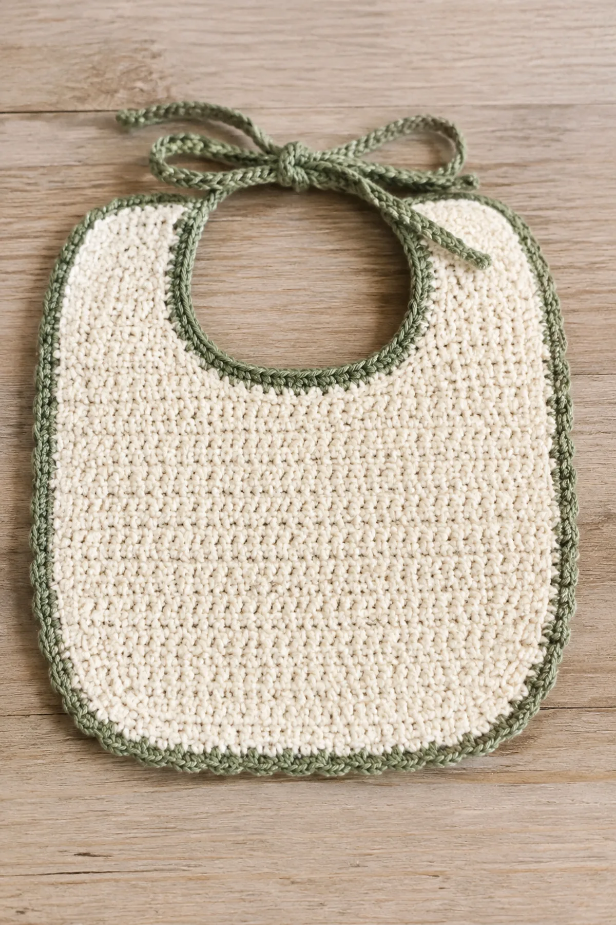 Finished easy crochet baby bib in soft cream and sage yarn on a neutral nursery surface