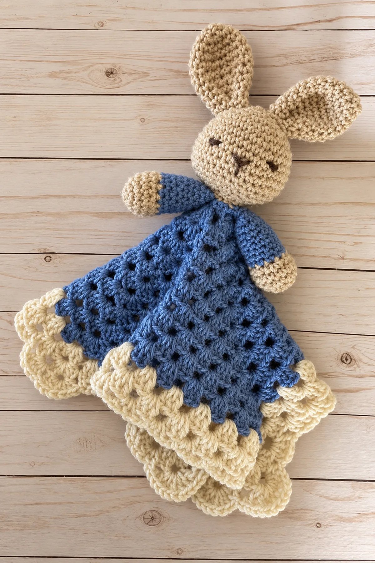 Oatmeal crochet bunny puppet attached to a denim blue cluster lovey with cream scalloped border