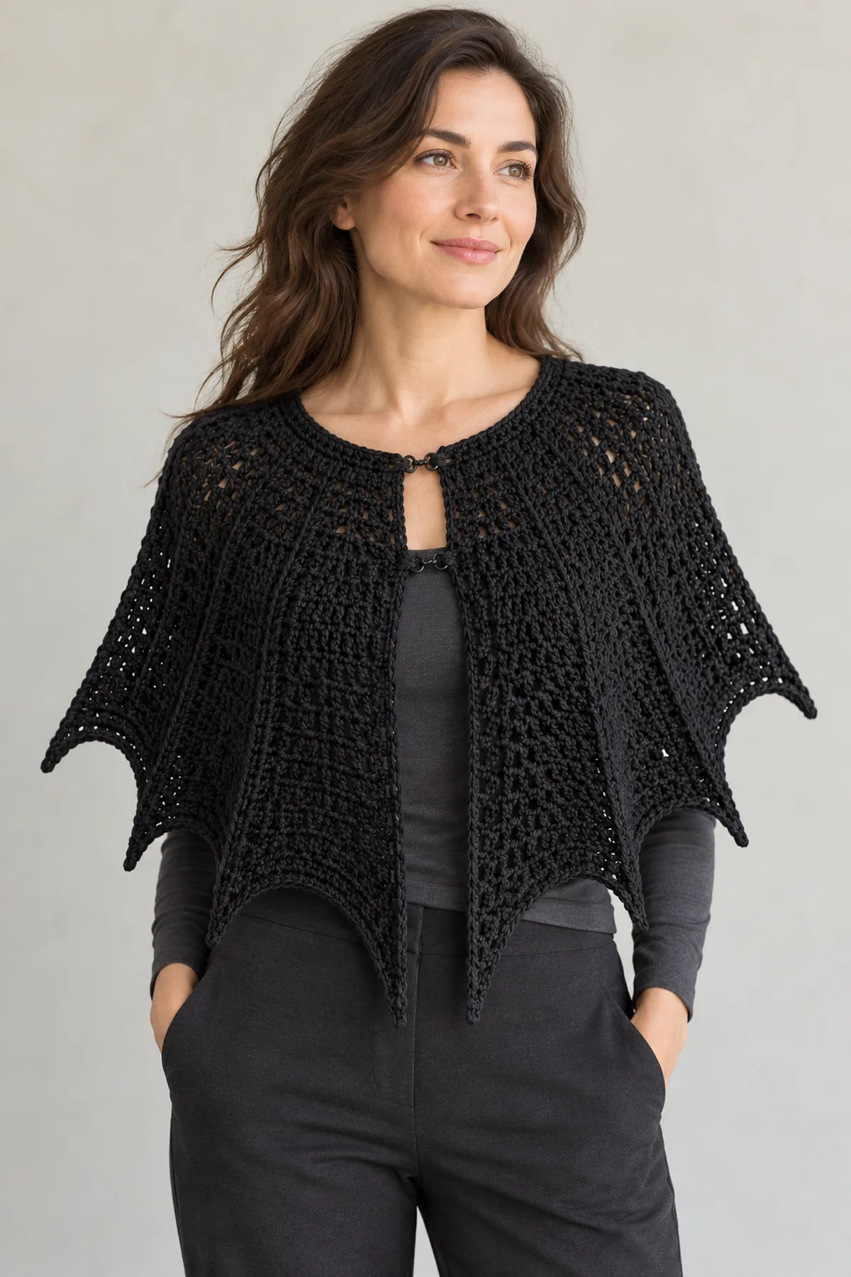 Adult wearing an original black crochet shoulder cape over plain charcoal outfit, six graduated batwing hem points and simple front neckline closure visible, autumn daylight