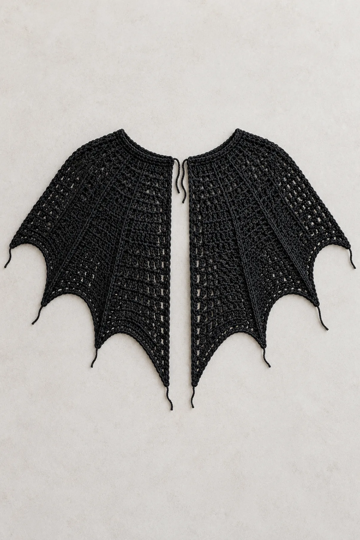 Black semicircular crochet cape laid flat with six separate tapered wing points, center pair longer, unfinished edges and unsewn front closure