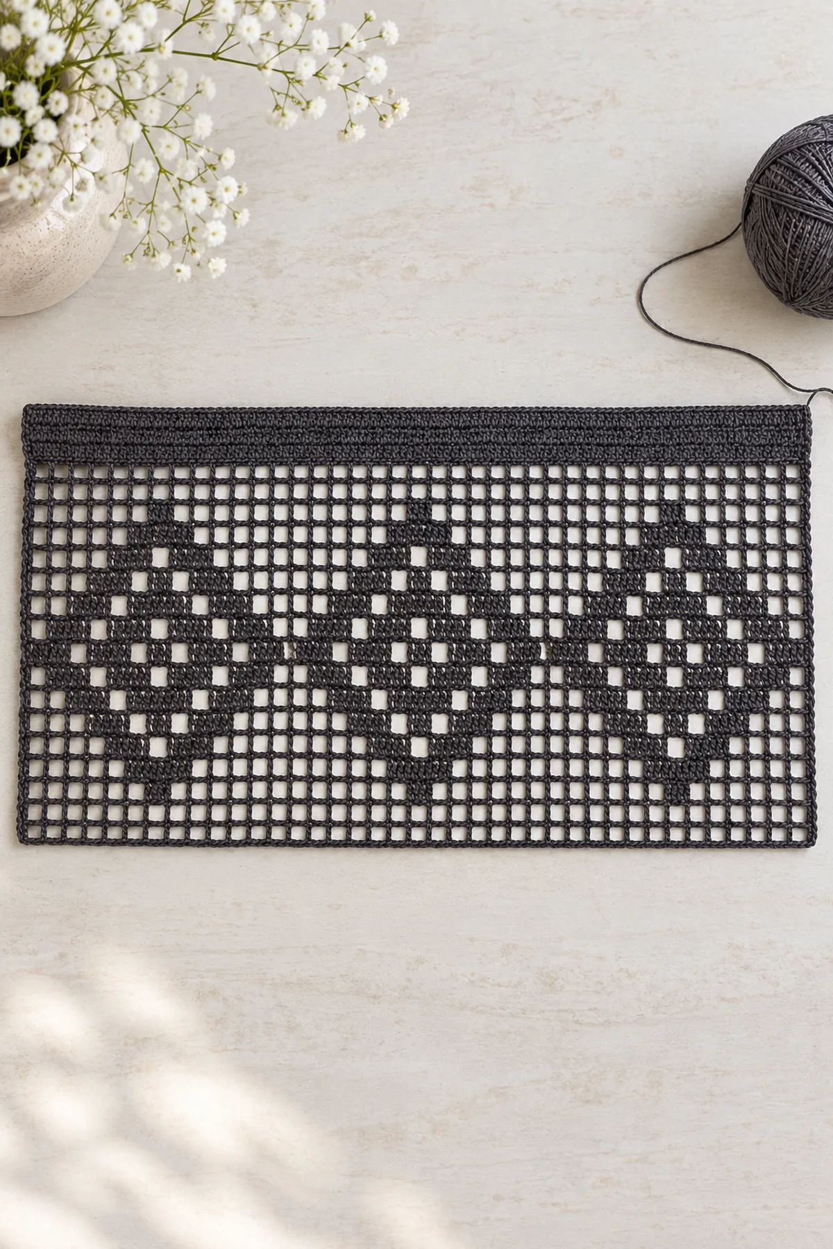 Flat completed charcoal open filet rectangle with three stepped diamond web motifs, solid straight header unfolded, lower edge still plain before tiny picots, pale table beneath mesh, no rod