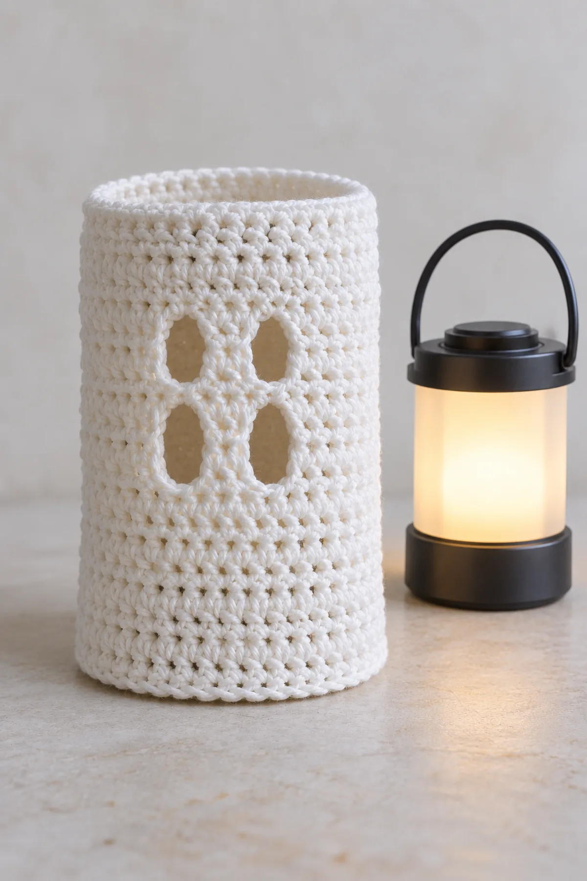 White ghost crochet panel sewn into a cylinder with a neat straight top rim, lower edge still plain before scallops, cool LED lantern standing separately
