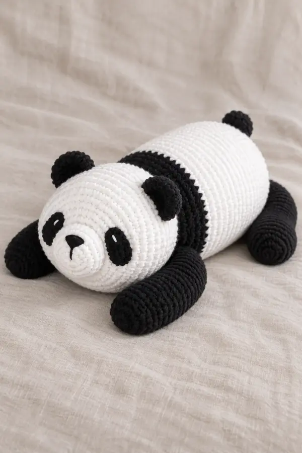 Large reclining black-and-white panda cub with a long horizontal white barrel, broad black shoulder band, large round white head, small black ears, oval black eye patches, white protruding muzzle, four elongated black paws and tiny black rear tail. Rounded embroidered nose, no hard eyes; reproduce the resting posture and proportions from the reference, not the existing seated red panda or lovey. Finished object only, original product photograph composition, no source text or logo.