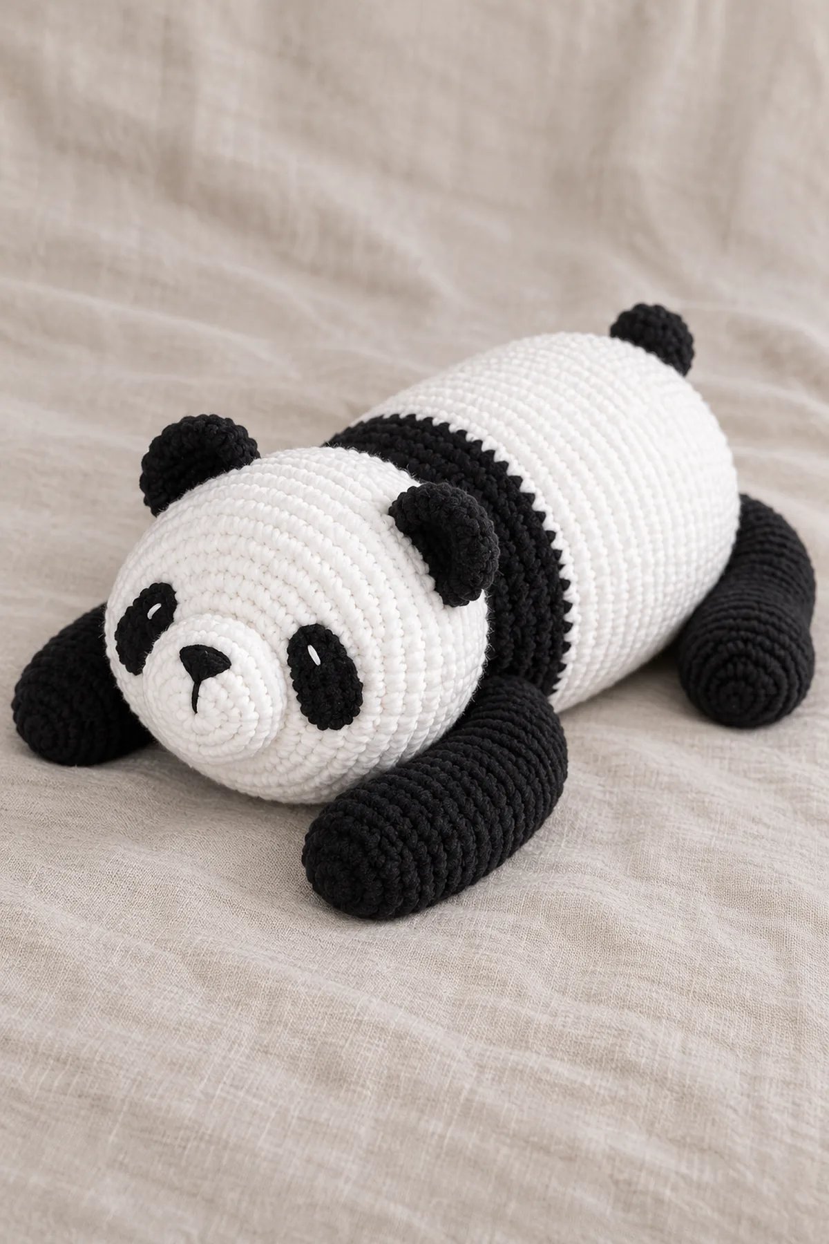 Large reclining black-and-white panda cub with a long horizontal white barrel, broad black shoulder band, large round white head, small black ears, oval black eye patches, white protruding muzzle, four elongated black paws and tiny black rear tail. Rounded embroidered nose, no hard eyes; reproduce the resting posture and proportions from the reference, not the existing seated red panda or lovey. Finished object only, original product photograph composition, no source text or logo.