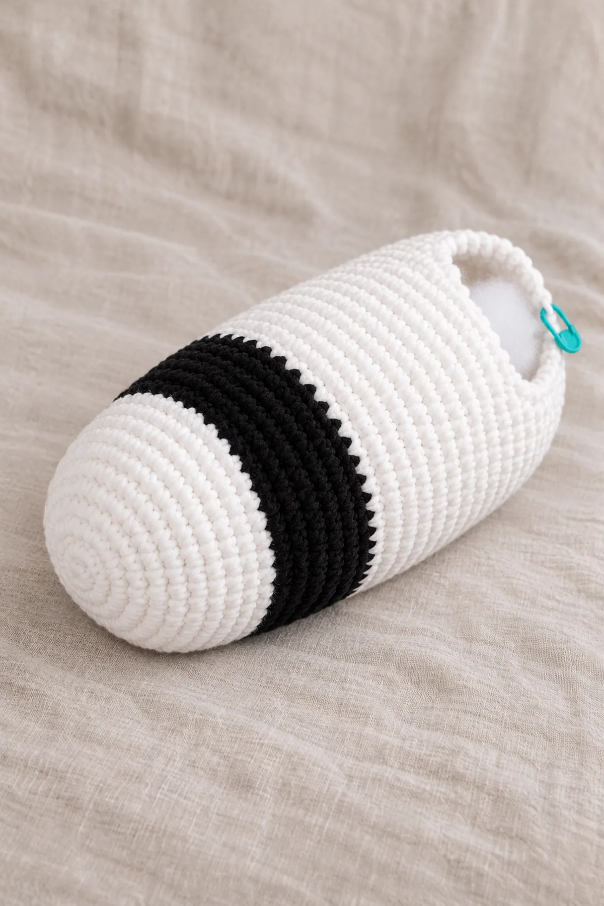 Unfinished long white plush-yarn panda barrel with one broad black shoulder band near its closed front, rear opening with a marker and visible white stuffing; no head or limbs attached.