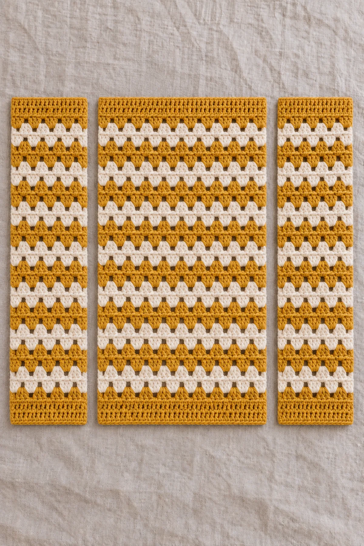 One unsewn mustard-and-cream baby cardigan back with sixteen repeating three-double-crochet cluster columns and two smaller matching fronts with eight cluster columns each, horizontal cream stripe rows aligned, no hood or sleeves.