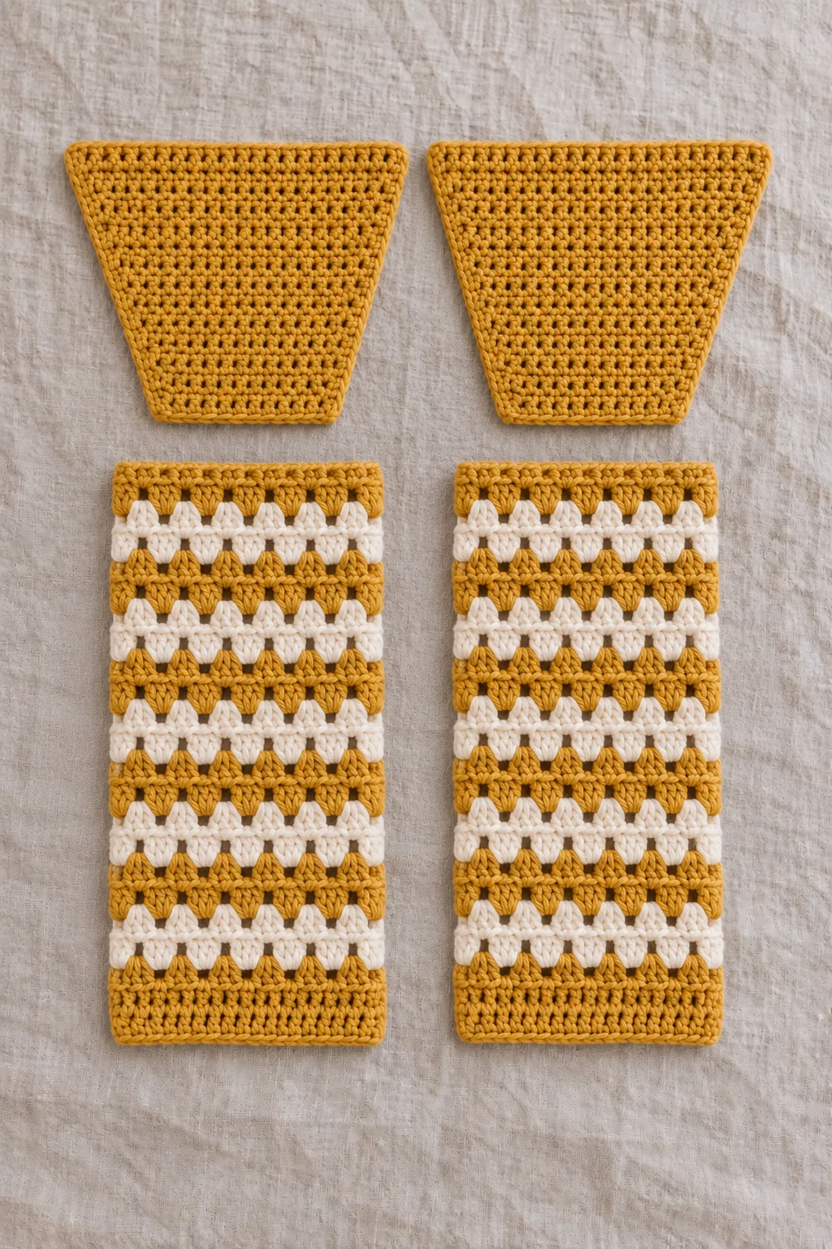 Two separate long mustard-and-cream granny-cluster sleeves and two separate plain mustard single-crochet shaped hood panels with wider crown edges than narrow neckline bases beside the unsewn body panels, no assembled garment.