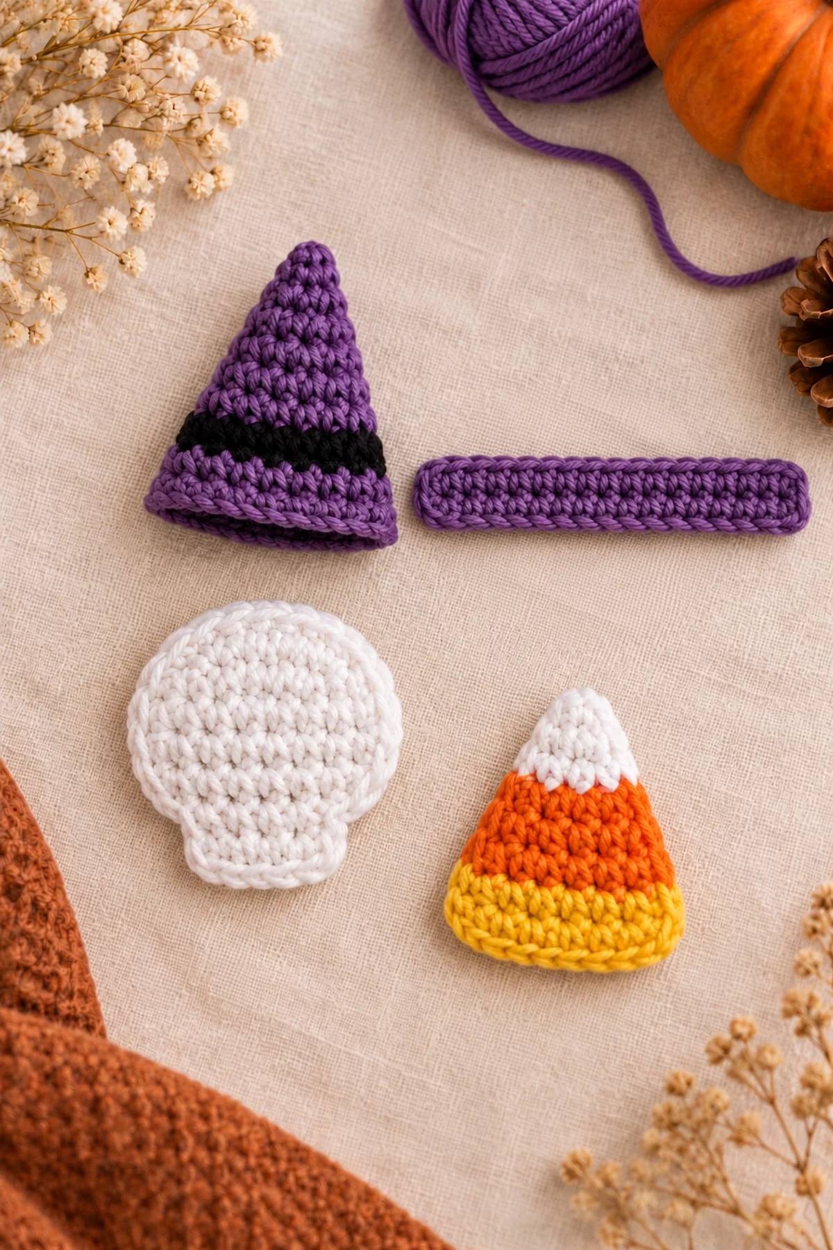 Unassembled flat crochet components on linen: purple tapered hat crown with one black base stripe and separate purple brim, white skull circle with short jaw, flat yellow orange white candy-corn triangle; no metal clips or finished faces yet.