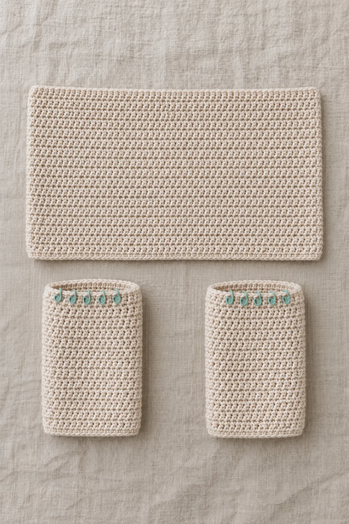 Flat oatmeal 80-stitch crochet cardigan body and two separate 30-stitch sleeve tubes before the six-stitch underarm holds