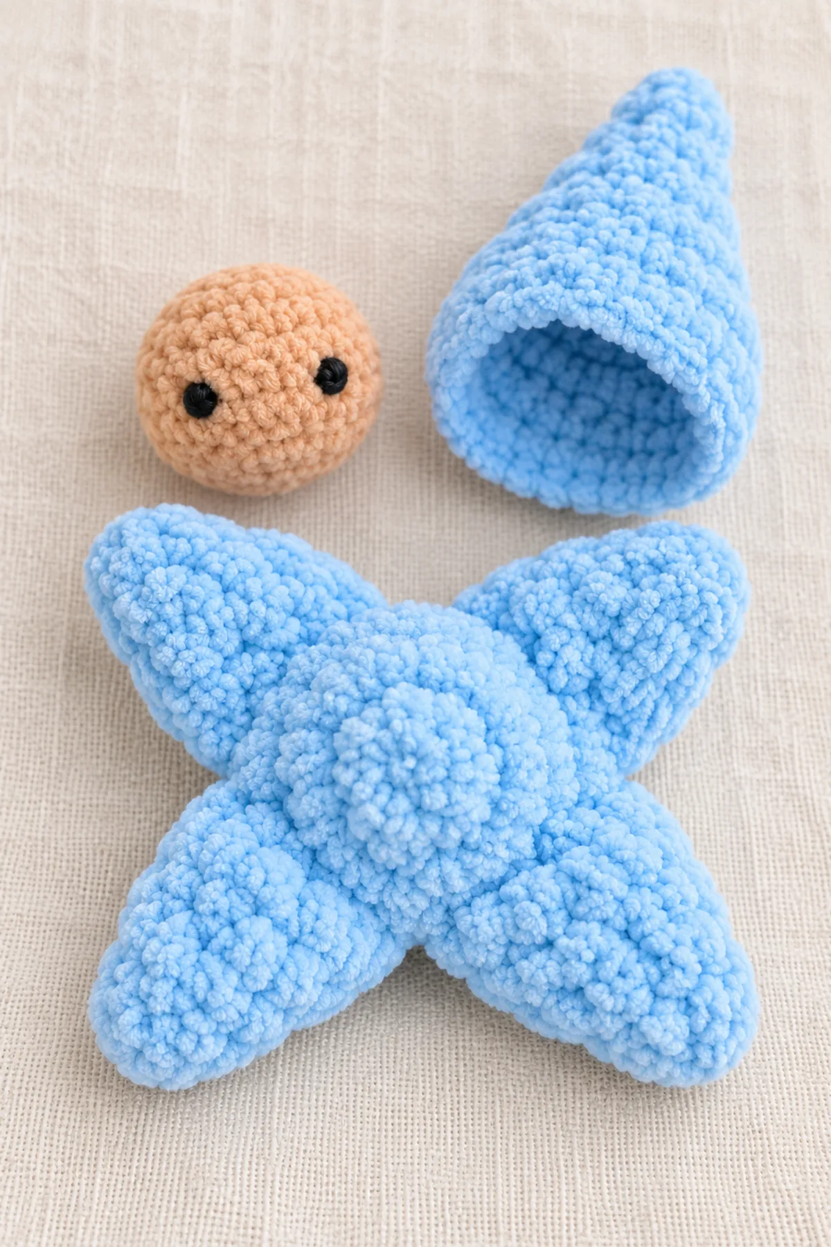 Completed shallow powder-blue four-point X body beside separate peach round embroidered face and separate powder-blue pointed cone hood with open circular rim, before fitting and head assembly.