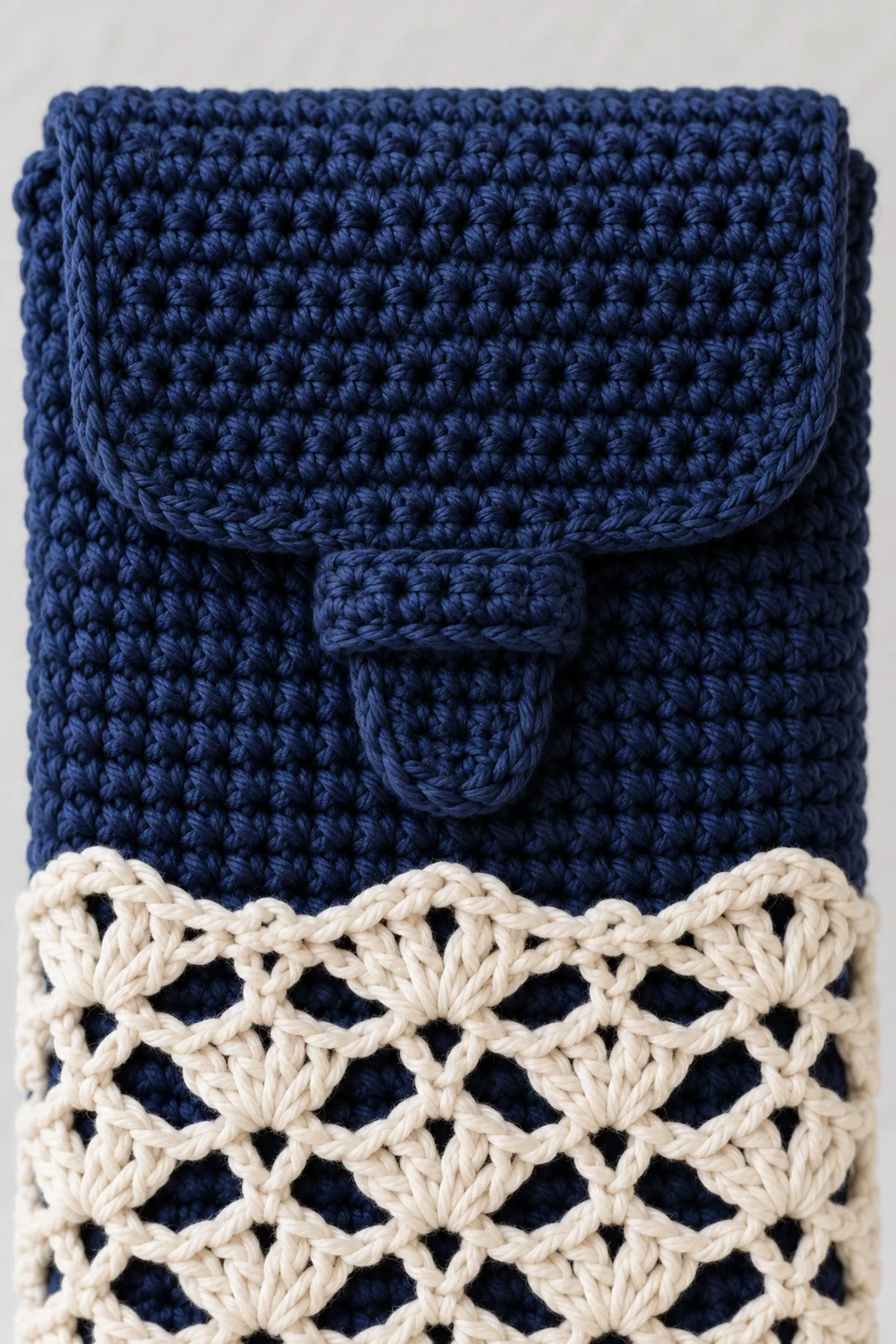 Close-up of navy integral flap tab sliding under an eight-stitch navy keeper sewn only at its short ends over cream crochet eyelet overlay, no button