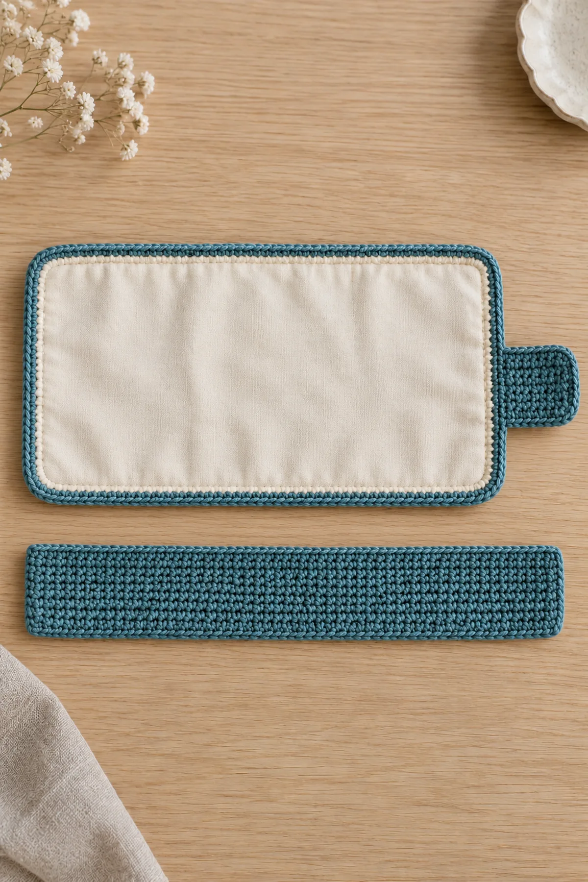 Full oat linen-stitch rectangle with cream lining and separate teal narrow pocket band beside it before sewing, no compartments or jewelry yet