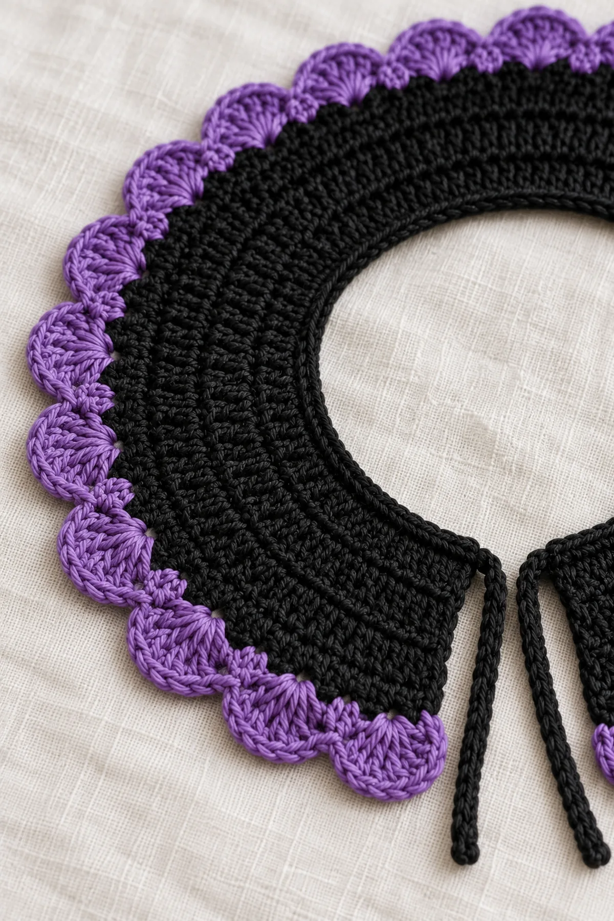 Macro of violet five-double-crochet fan scallops anchored on black hdc collar edge, clear yarn fibers and single sc valleys, small piece of narrow black neckline visible behind; no knots or beads