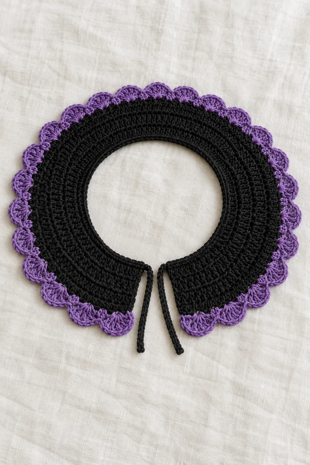 Original adult open-front crochet collar laid flat in a shallow C-shaped crescent on ivory linen. Narrow black neckline, four expanded rows of black half-double crochet, single violet border of many small five-dc fan scallops, two short narrow flat black ties at neckline ends. No brooch, buttons, beads, web mesh, long scarf or person