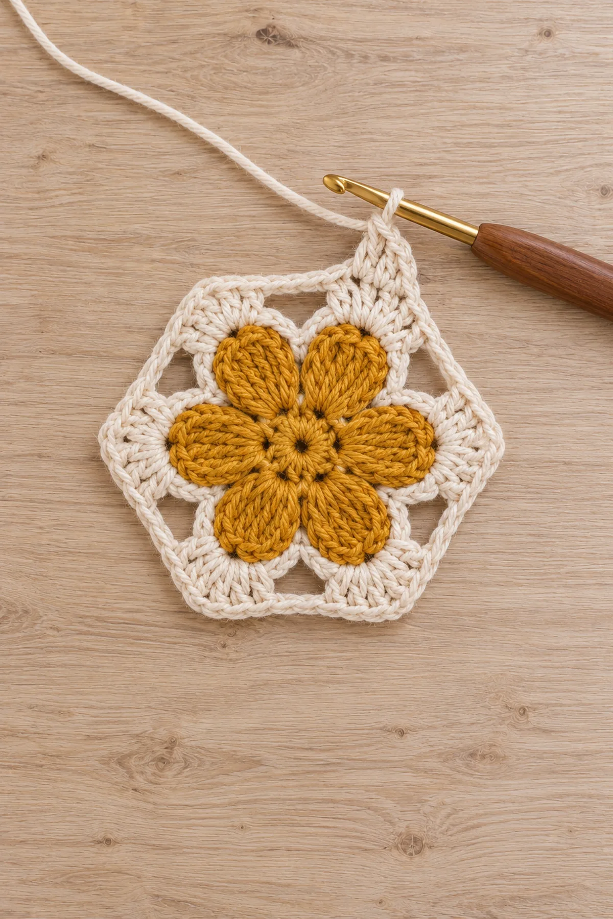 One unfinished flat crochet daisy motif: mustard six-petal center and cream chain arches being framed into six corners, hook at working edge, no other flowers or long runner