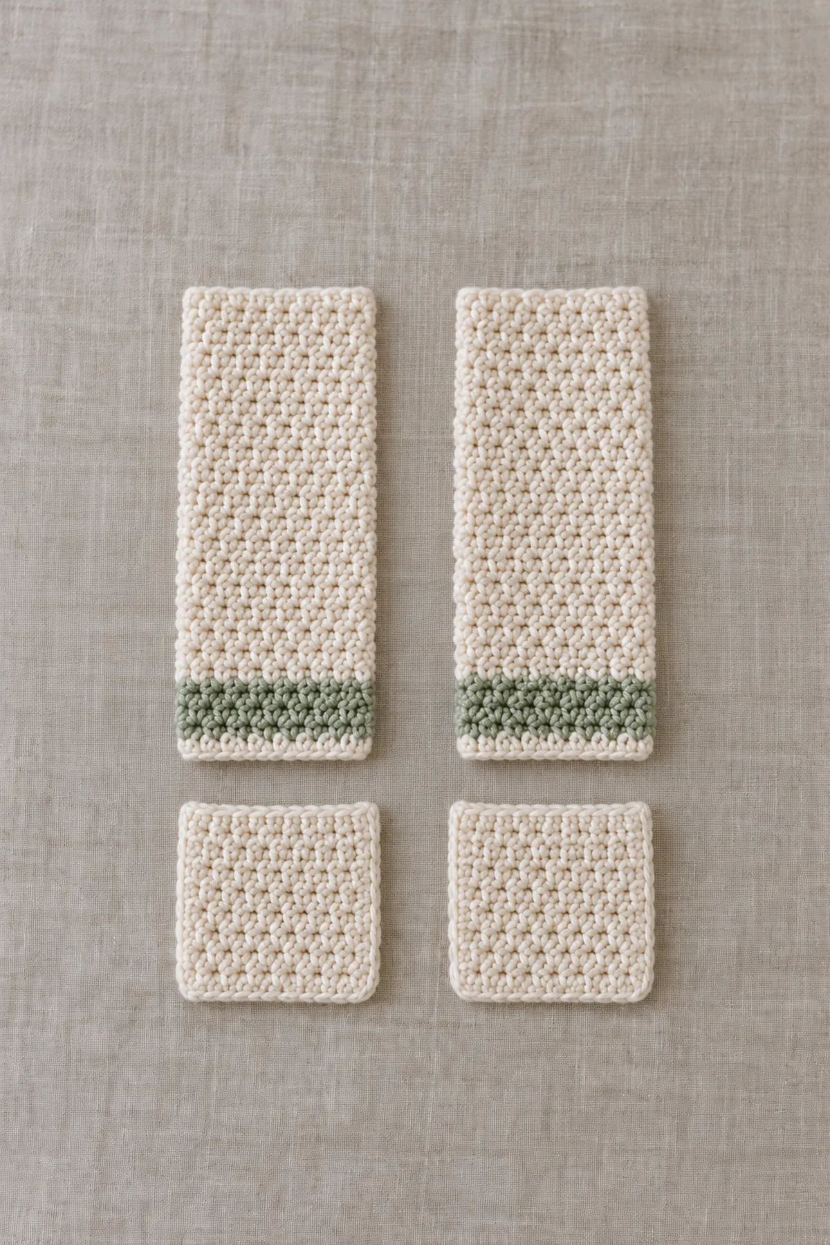Two plain cream straight crochet sleeves with small sage cuff bands and two separate small cream square patch pockets beside three matching body panels; parts are unsewn.
