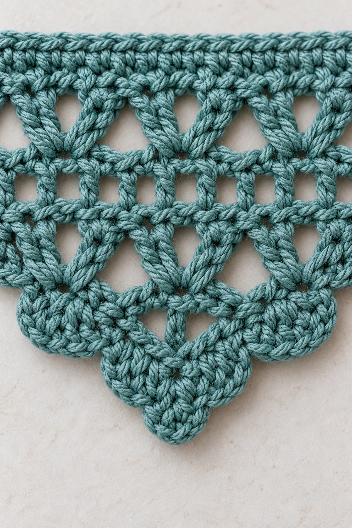 Macro of muted-teal crochet bandana fabric showing one solid V-stitch of two double crochets and a chain gap, adjacent tiny eyelet row and restrained three-hdc lower scallop