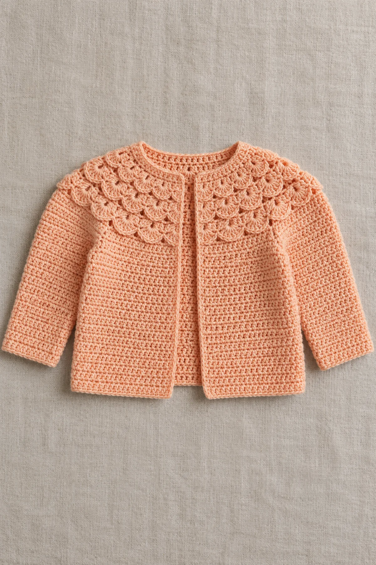 Original soft-apricot open-front long-sleeve crochet baby cardigan with a wide integrated graduated fan-shell round-yoke crown on cream linen