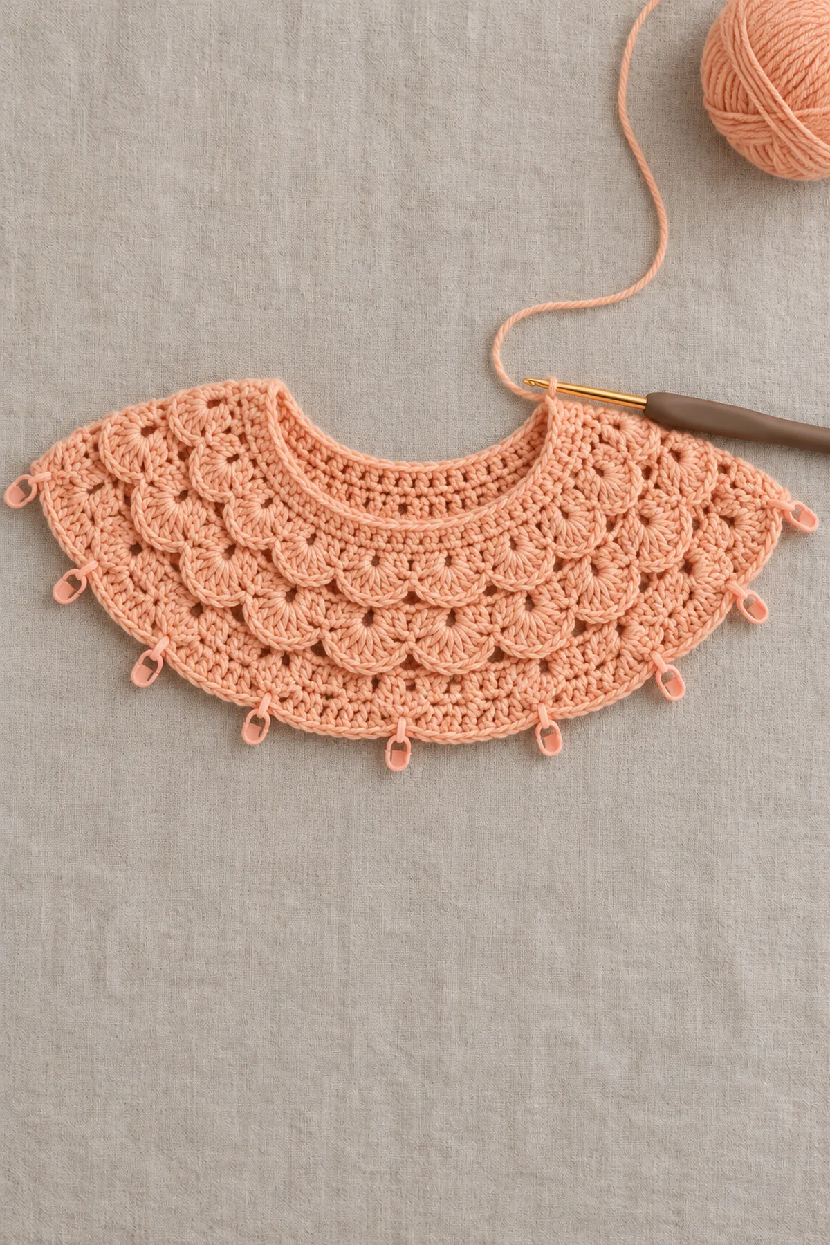 Top-down baby cardigan yoke in progress showing twelve graduated apricot crochet fan-shell repeats expanding around the neckline