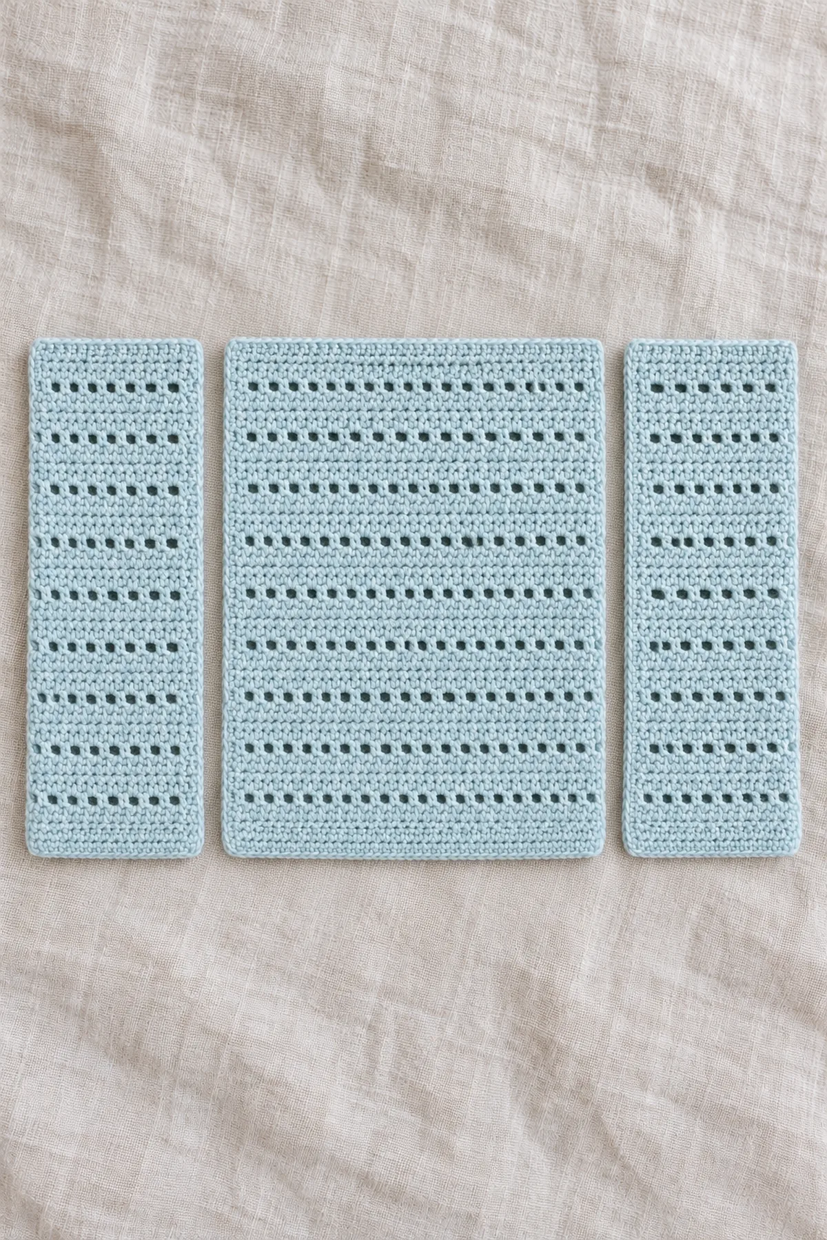 Three separate perfectly rectangular pale sea-glass blue crochet body panels, one wide back and two narrow equal fronts; visible alternating rows of tiny eyelets and solid rows, square corners, no armhole cutouts or sleeves.
