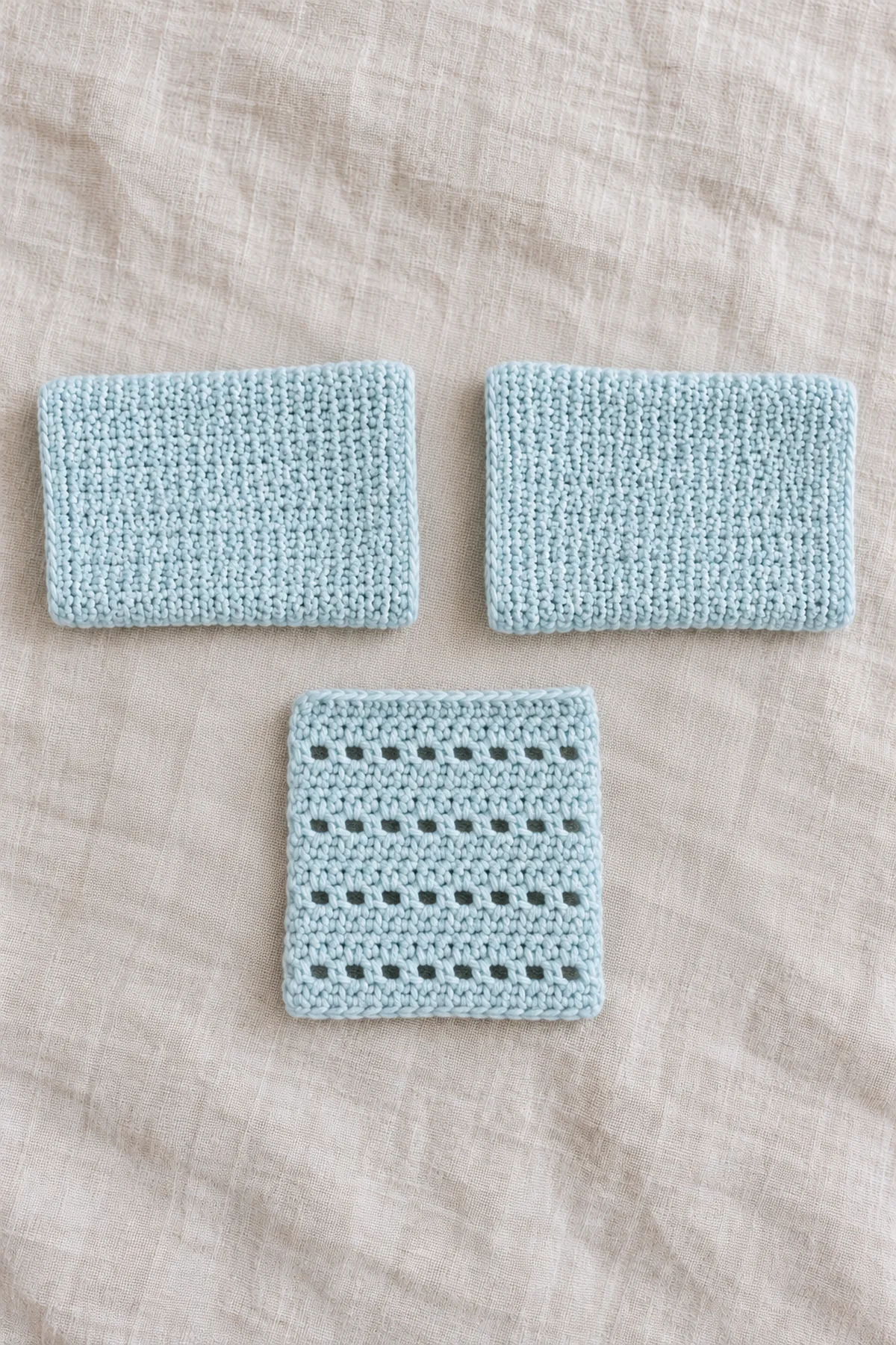 Two separate very short plain solid pale-blue hdc sleeve rectangles beside one small eyelet swatch; not joined to body, no finished cardigan.