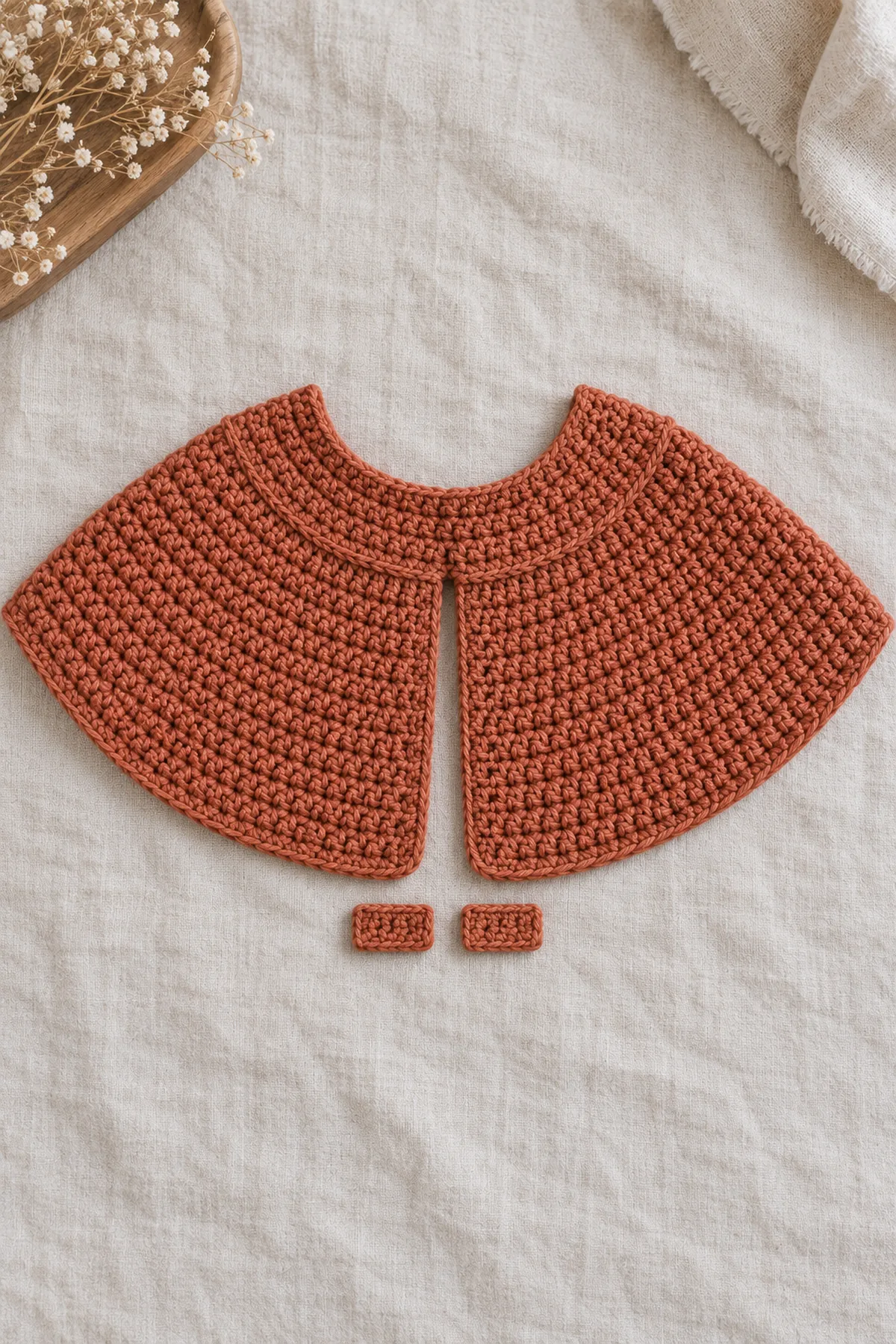 Terracotta crochet capelet body laid flat as open crescent after six increase rows and even length rows, unfinished raw neckline and two separate short flat tab strips beside it; no collar sewn yet.
