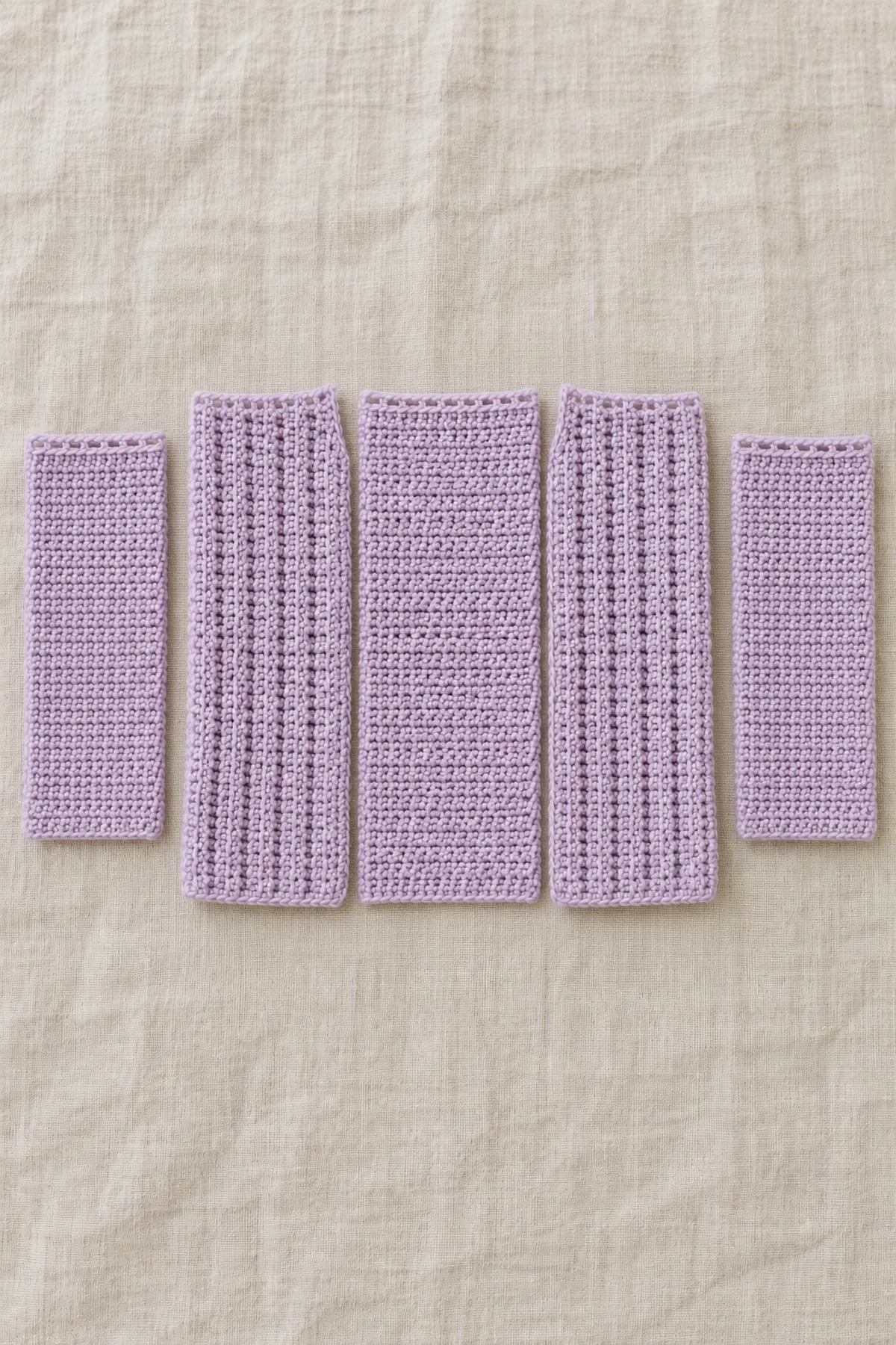 Two separate smooth plain lilac crochet rectangular sleeves beside three sideways rib body panels, marked sleeve upper foundation edges, no cuffs folded or pieces joined.