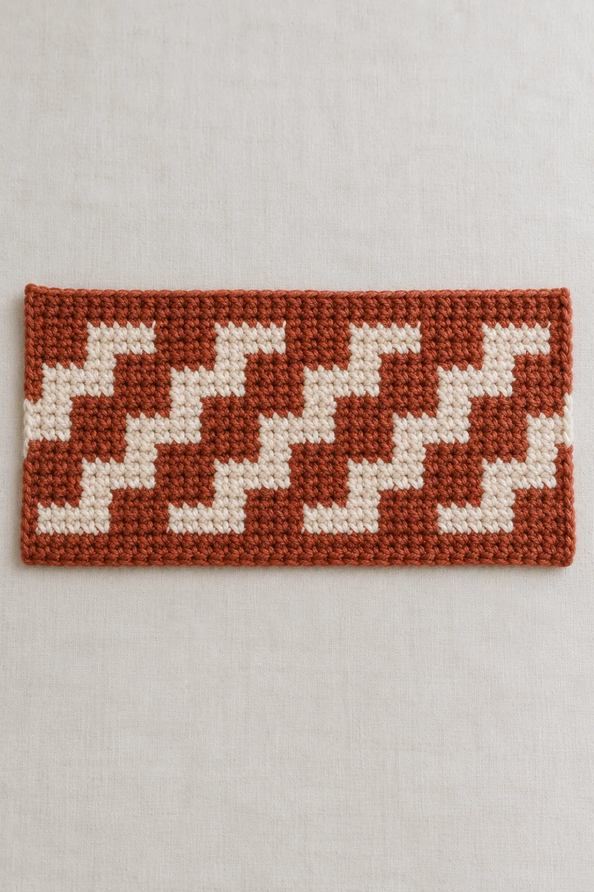 Completed rust-and-cream 104-stitch wide flat mosaic rectangle with offset staircase pattern, short side edges ready to seam, no borders yet