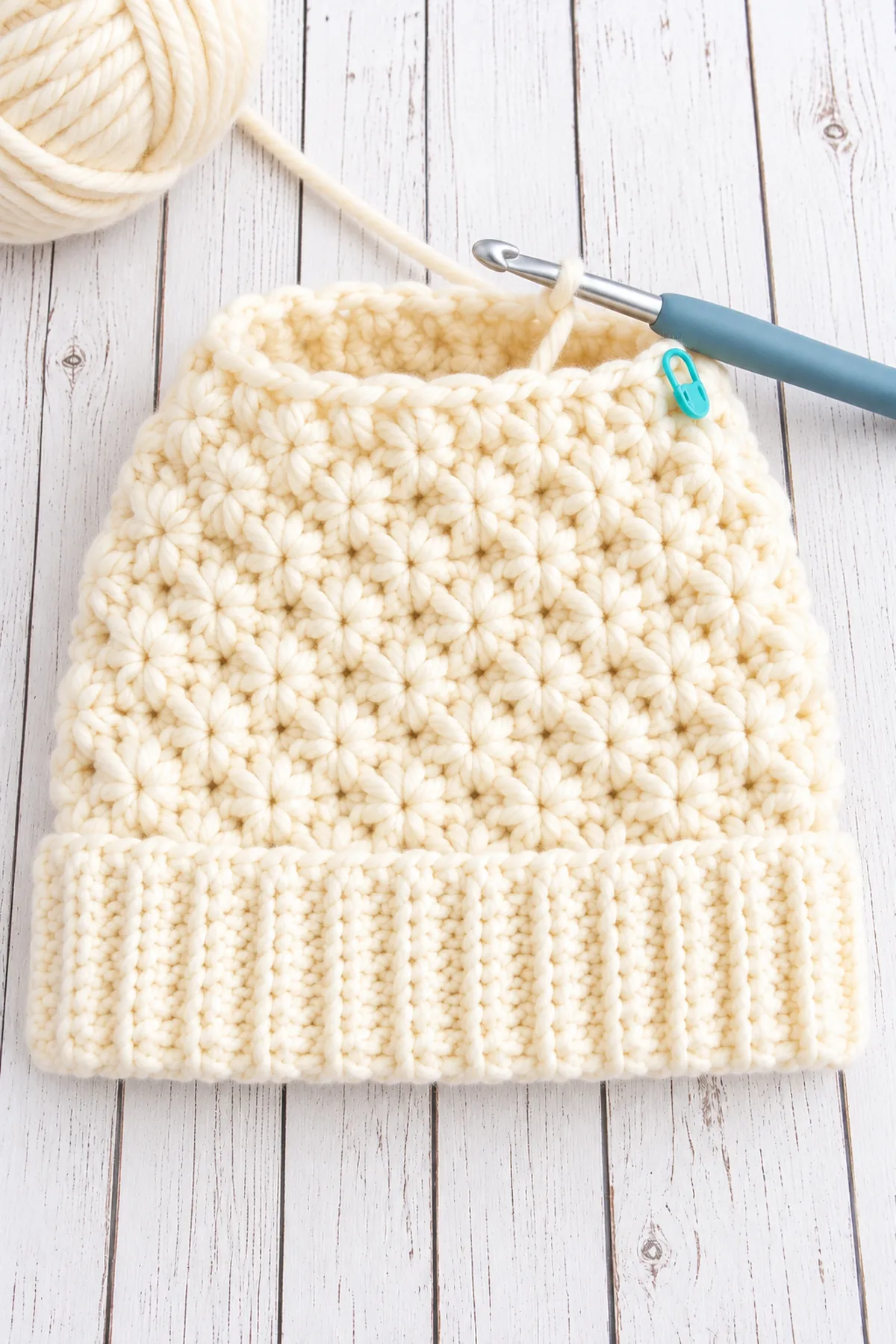 Cream beanie body rising from joined ribbed brim with visible 72-stitch star-cluster rounds before crown decreases.