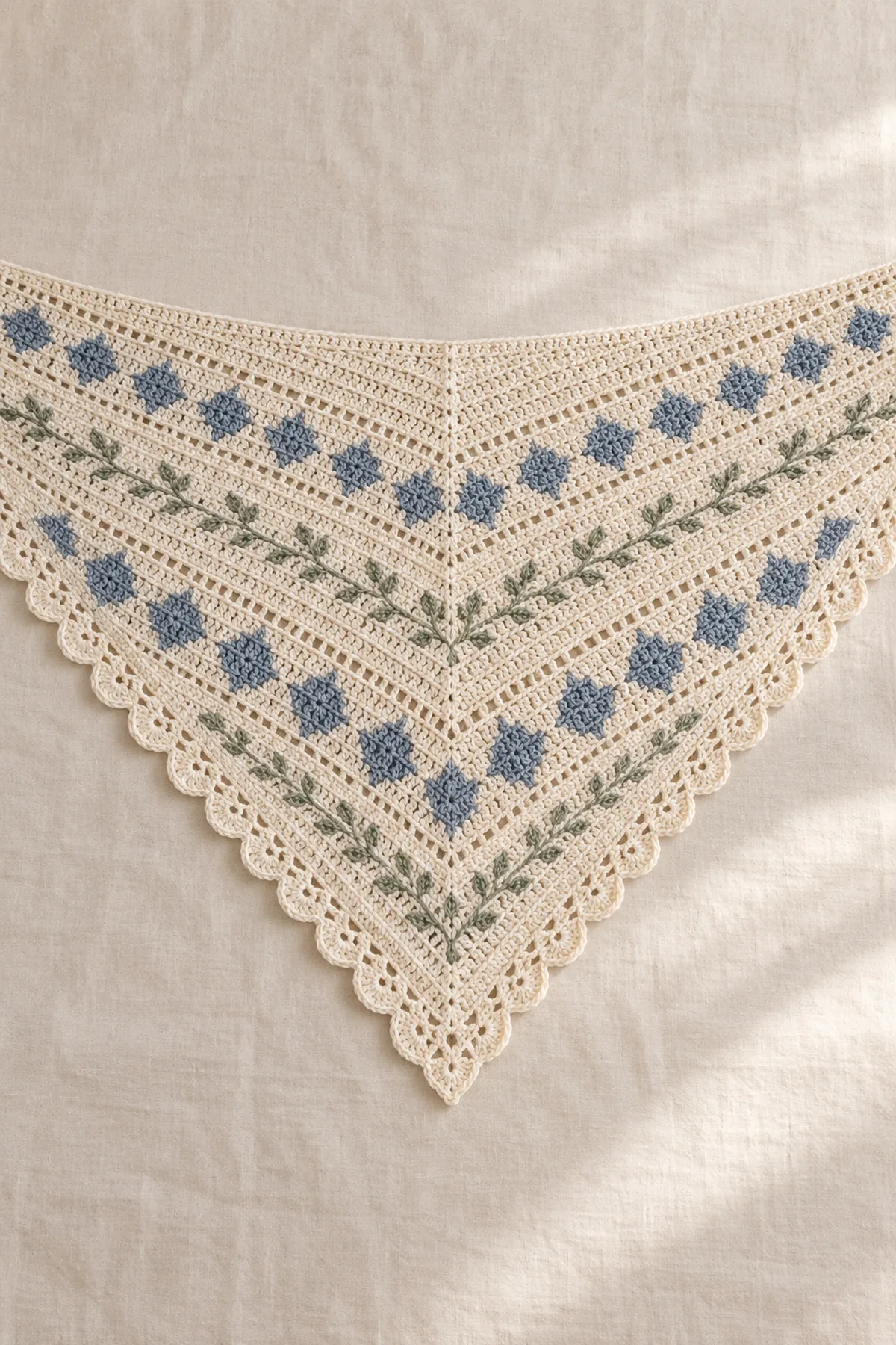 Cream crochet triangle shawl with slate-blue diamonds, sage sprigs and scalloped edge